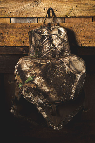 Spring Thunder Turkey Vest in Realtree APX camo hanging on wood backdrop, rear view with large fold-down seat cushion visible.