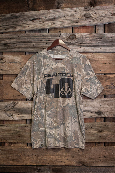Realtree 40th Anniversary Jersey tri-blend camo short sleeve shirt hanging on wooden backdrop with bold “Realtree 40” front graphic main