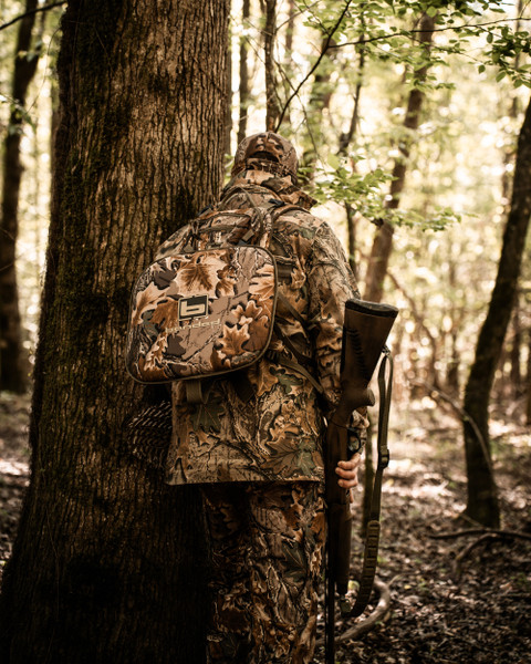 Rear view of hunter with Air Elite camo turkey vest and shotgun in forest.