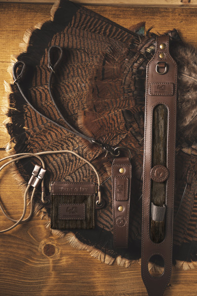 Flat lay of the Wren & Ivy Realtree 40th Anniversary Call Pouch with coordinating leather hunting accessories.