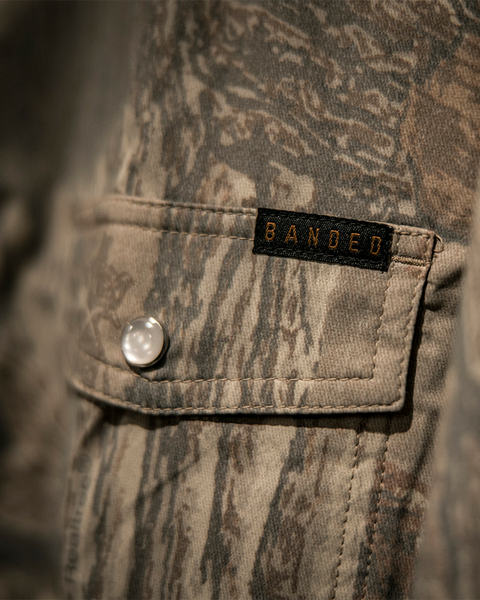 Close-up of Banded logo tag on Realtree Xtra Grey camo shirt pocket.