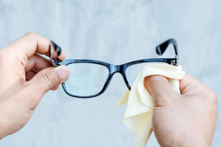 Hands cleaning blue wayfarer style glasses with white glasses cleaning cloth