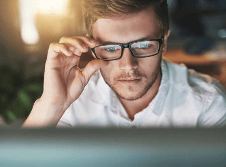 Man on computer wearing rectangular black bold framed blue light blocking glasses