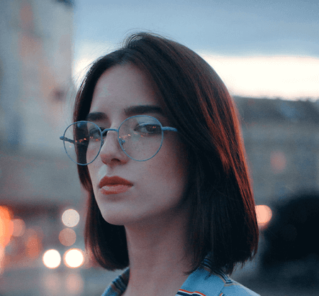 Young woman wearing blue round wire frame glasses with cityscape background