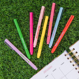 Eight colorful felt tip markers with motivational quotes scattered on green grass next to an open January planner page.