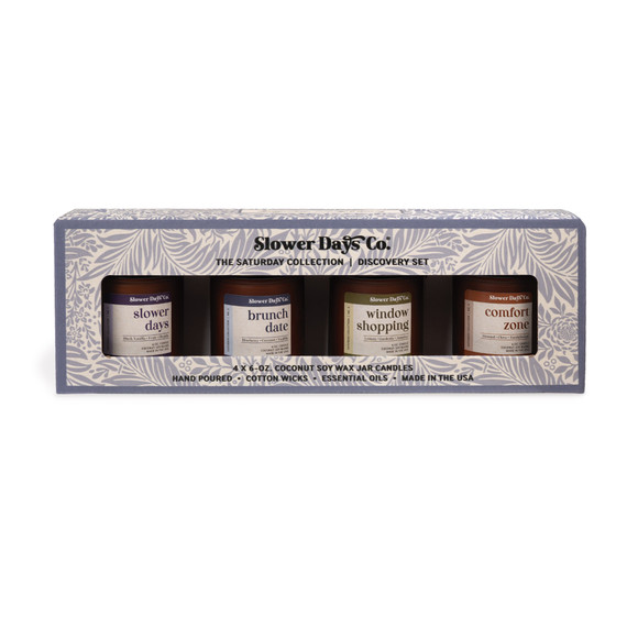 A gift box containing four 6 oz. amber glass jar candles from Slower Days Co., labeled Slower Days, Brunch Date, Window Shopping, and Comfort Zone.