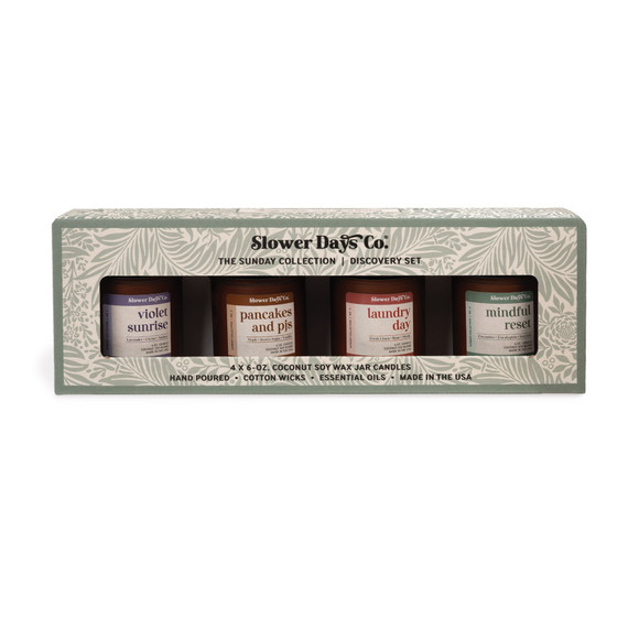 A gift box containing four 6 oz. amber glass jar candles from Slower Days Co., labeled Violet Sunrise, Pancakes & PJs, Laundry Day, and Mindful Reset.