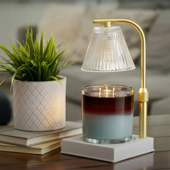 The Gold Luna Candle Warmer Lamp styled on a wooden coffee table, warming a jar candle next to a potted green plant and a stack of books