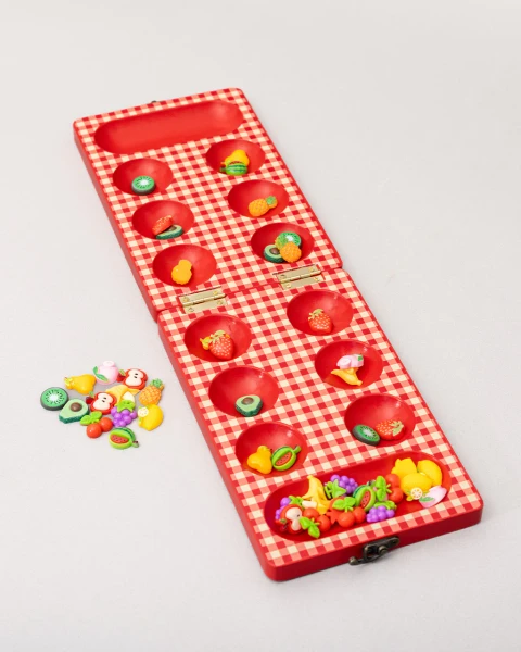 Open wooden mancala board with red and white checkered pattern and pieces shaped like fruit