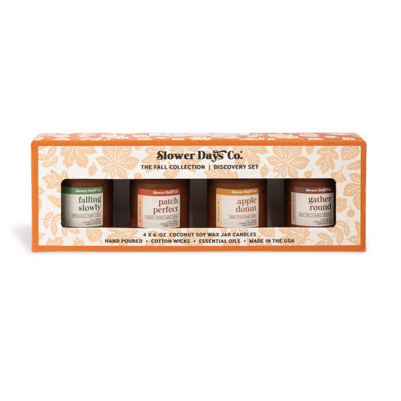 A gift box containing four 6 oz. amber glass jar candles from Slower Days Co., labeled Falling Slowly, Patch Perfect, Apple Donut and Gather Round.