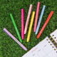 Eight colorful felt tip markers with motivational quotes scattered on green grass next to an open January planner page.