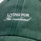 Close-up of white "Living for the Weekend" embroidery on textured, faded green cotton fabric.