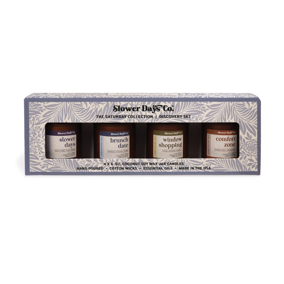 A gift box containing four 6 oz. amber glass jar candles from Slower Days Co., labeled Slower Days, Brunch Date, Window Shopping, and Comfort Zone.
