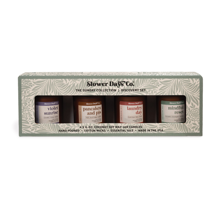 A gift box containing four 6 oz. amber glass jar candles from Slower Days Co., labeled Violet Sunrise, Pancakes & PJs, Laundry Day, and Mindful Reset.