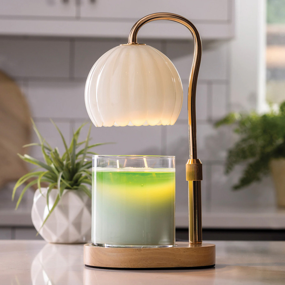 The Milk Glass Candle Warmer Lamp styled in a bright room, warming a jar candle on a marble tabletop next to a stack of books and a small potted succulent