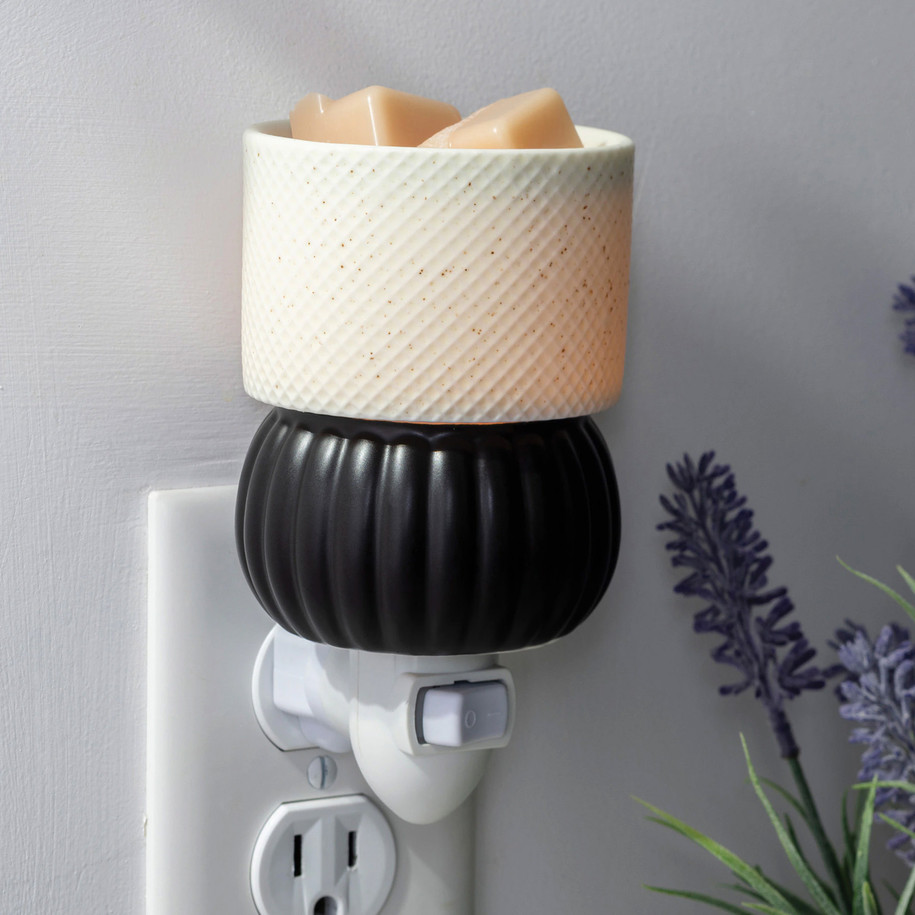 A close-up of the Luxe Lamp Pluggable Warmer in a cozy room, highlighting the diamond-textured ceramic shade and the removable top dish filled with green wax melts