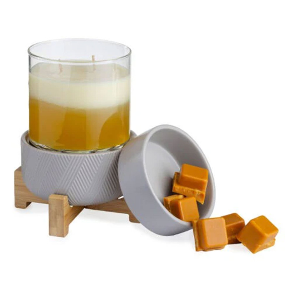 A 2-in-1 classic wax warmer with a grey herringbone textured base and wooden pedestal, shown warming a glass jar candle with a separate ceramic dish for wax melts resting alongside it
