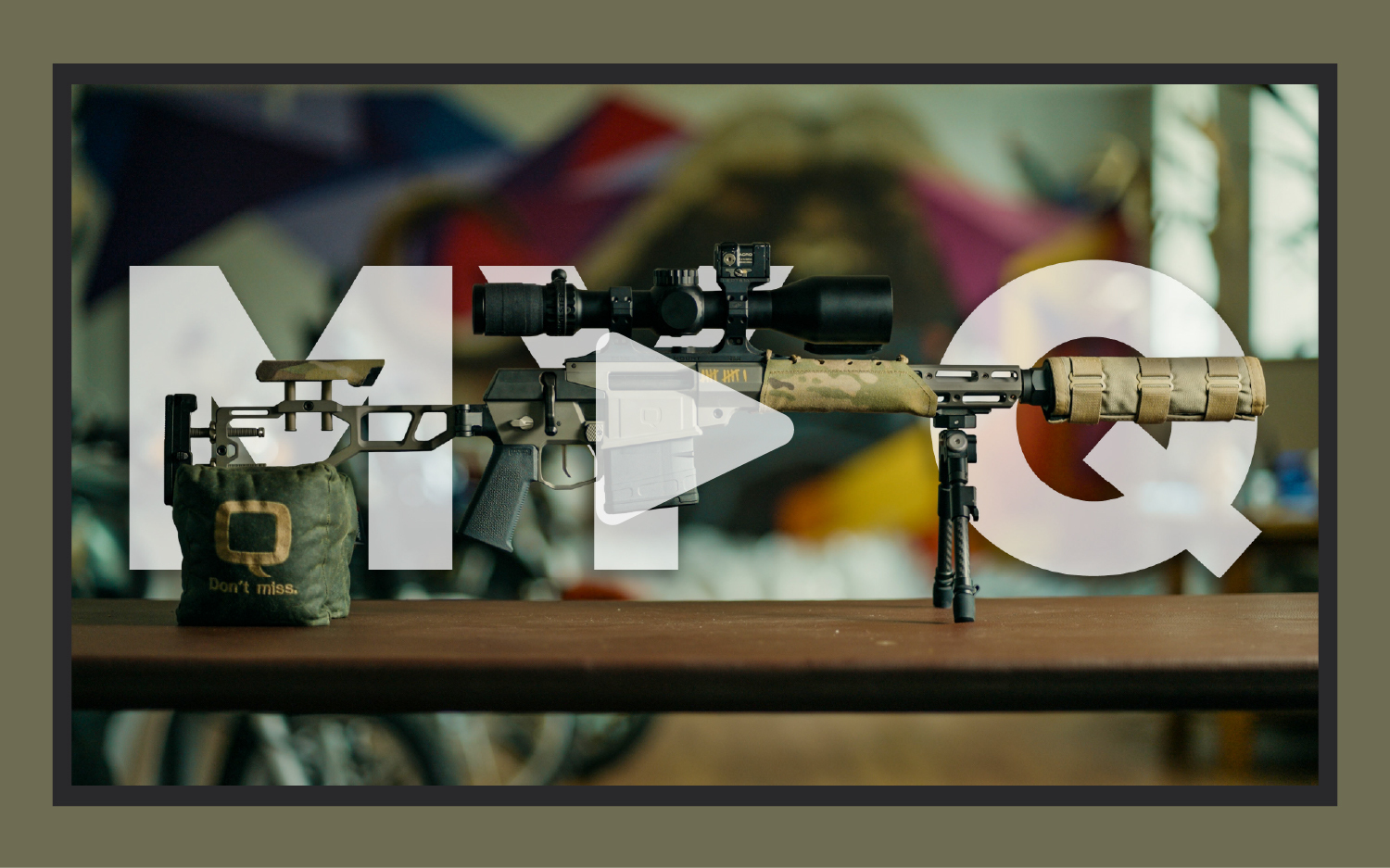 The Fix rifle by Q resting on a bipod and rear support bag with suppressor and optic, overlaid with large transparent MQ logo and play button.