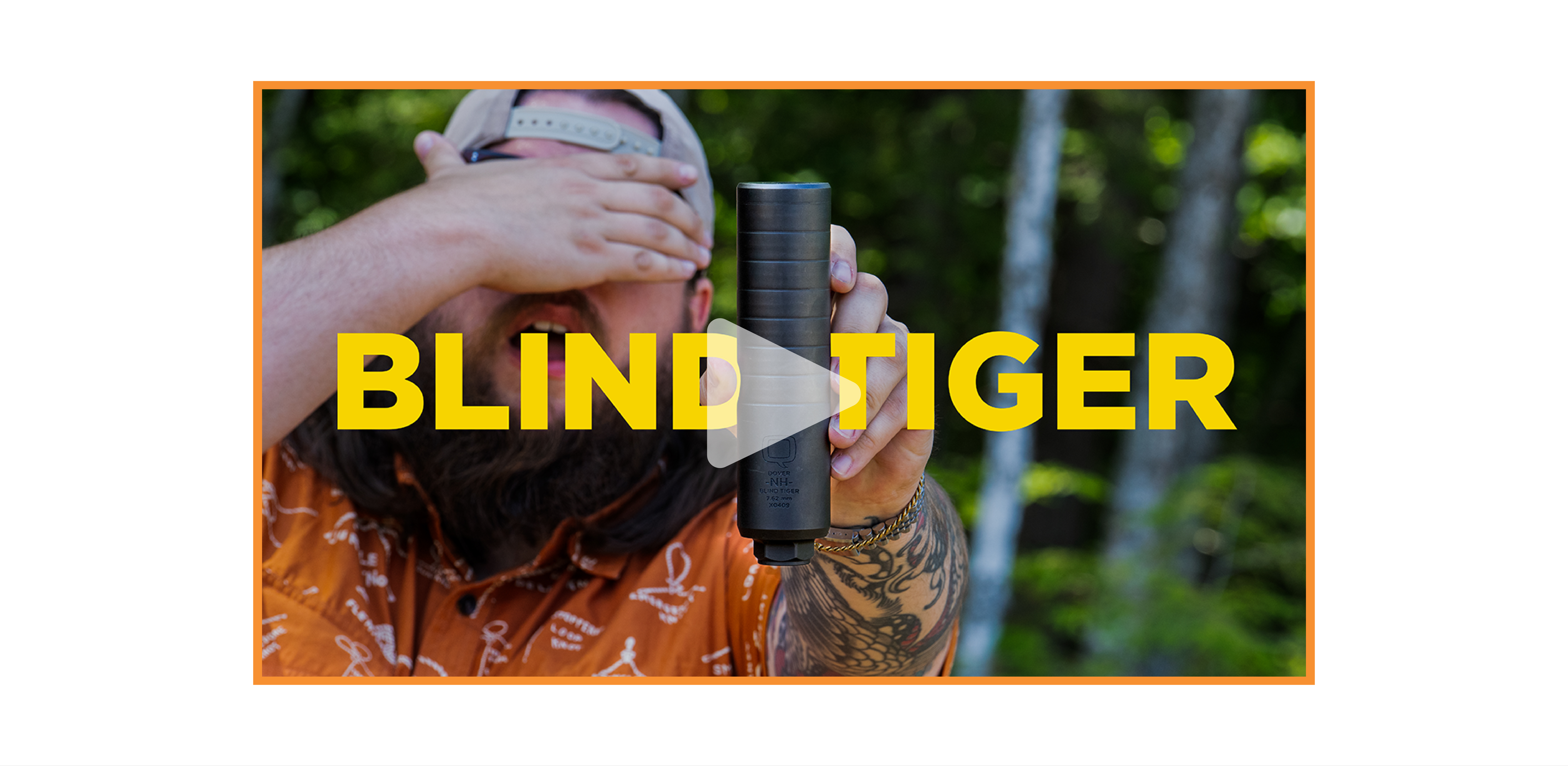 Man in an orange shirt and backwards hat holds up the Blind Tiger suppressor toward the camera, partially covering his face with one hand. The word “BLIND TIGER” is overlaid in bold yellow text, with a play button icon in the center, indicating a video thumbnail. Trees and greenery are blurred in the background.