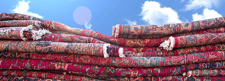 Stack of folded hand-knotted Persian rugs with red and navy floral patterns