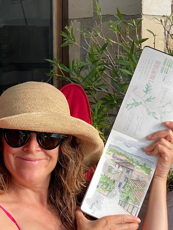 Alix, the teacher, holding one of her paintings and wearing a straw hat