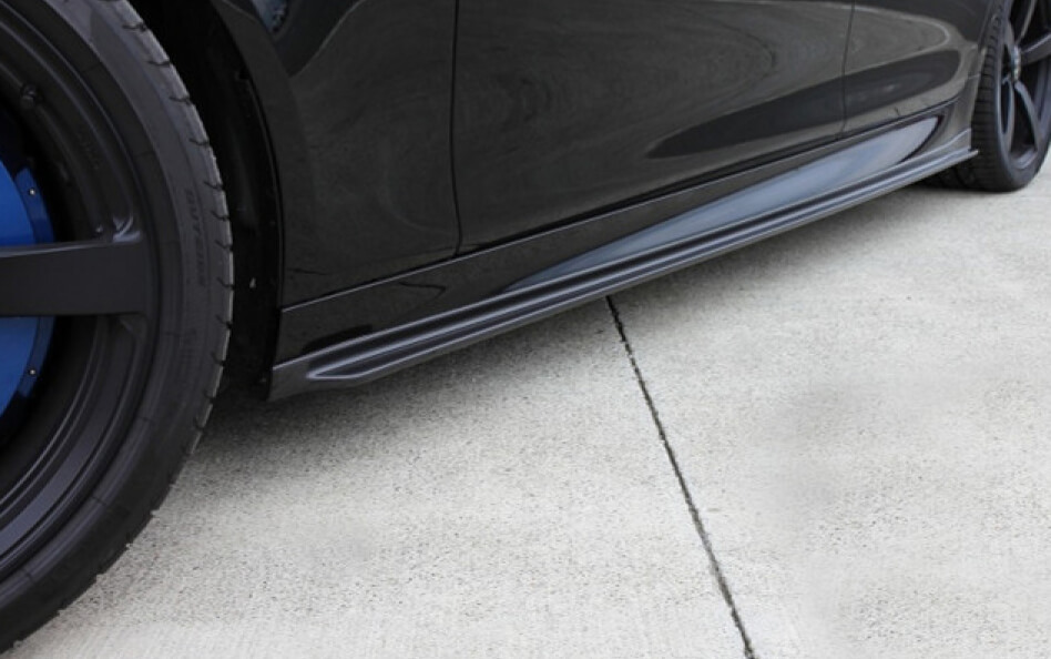 Close-up of a black BMW's side skirt, highlighting an aftermarket aerodynamic side splitter.