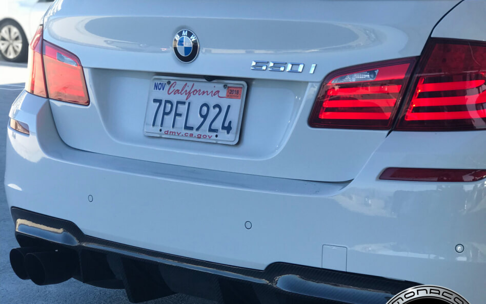 Rear view of a white BMW 530i that features red LED taillights, a dual exhaust system with black tips, and a carbon fiber rear diffuser.