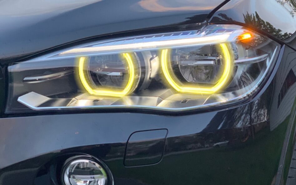 Close-up of a BMW headlight with illuminated yellow LED halo rings and amber turn signal.