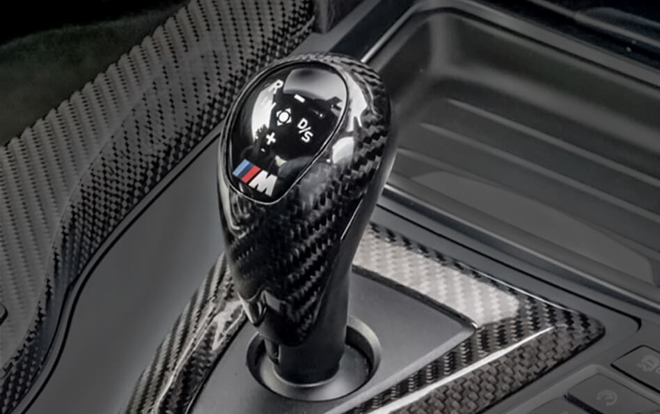 Close-up of a BMW M carbon fiber gear shifter with the M badge in the center console.