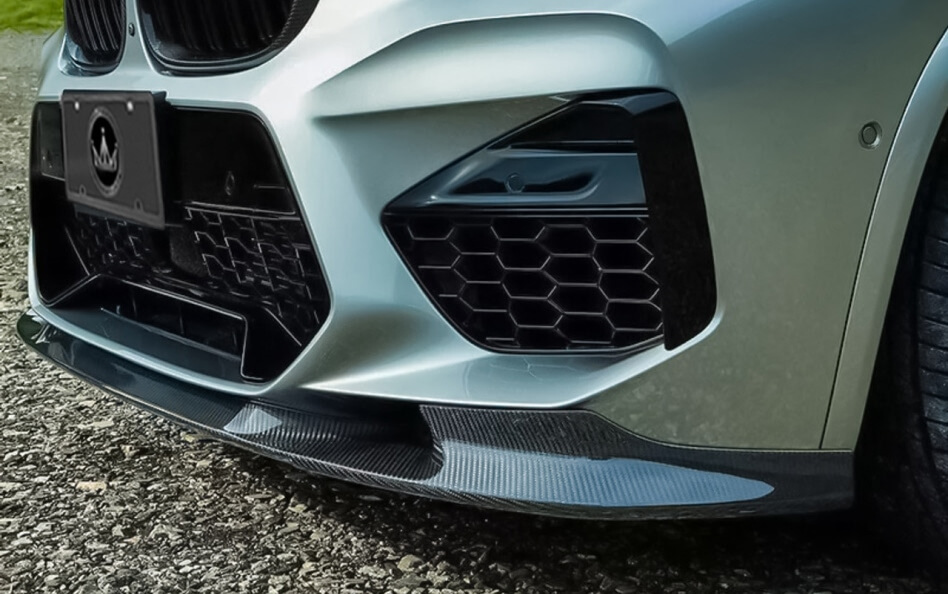 Close-up of a silver BMW front bumper with carbon fiber splitter and black honeycomb grille.