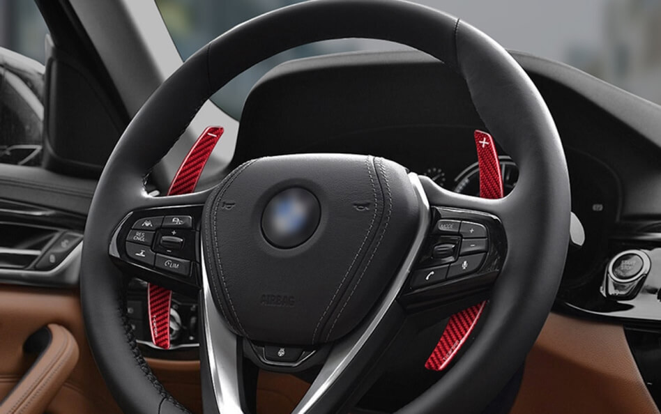 BMW steering wheel with red paddle shifter extensions and multifunction control buttons.