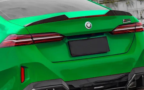 Green BMW G90 M5 with distinctive rear design and spoiler.
