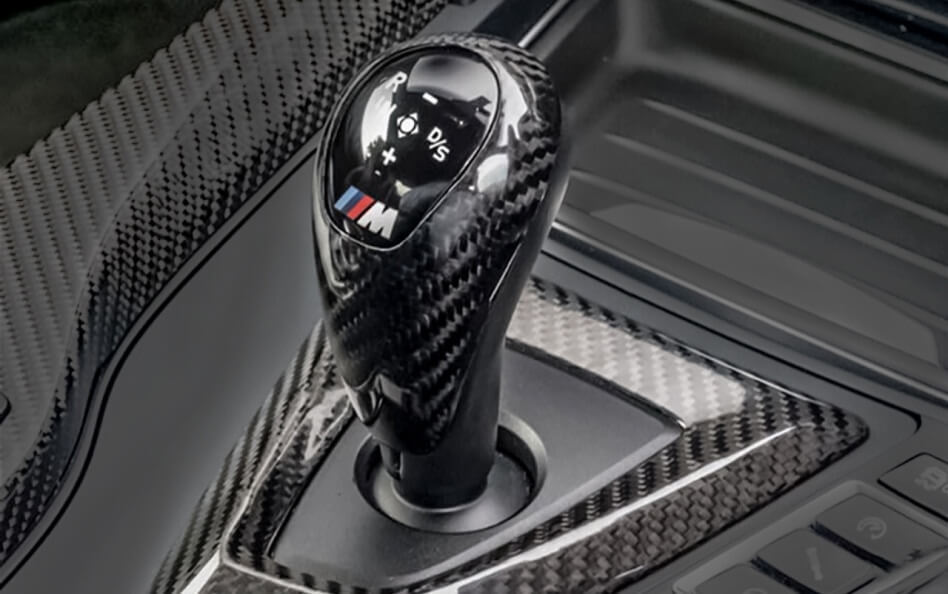 Carbon fiber BMW M gear shift knob with M tri-color logo on a matching carbon fiber center console.