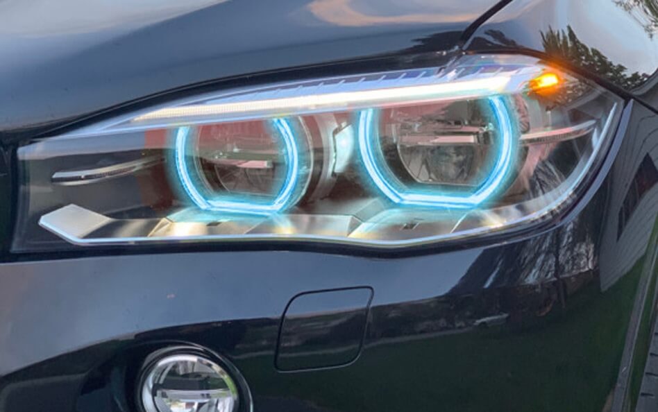 Close-up of a BMW headlight with illuminated blue LED angel eyes and amber turn signal.