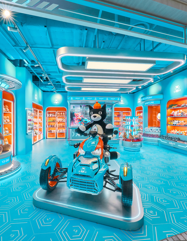 Jellycat Jack rides a futuristic vehicle inside a turquoise Jellycat store with bright shelving displays.