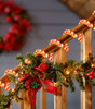 Candy cane rope light decorating a porch railing with Christmas garland and red bows