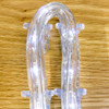 Clear LED rope lights bent into a U-shape and secured with small transparent clips, glowing with cool white light on a wood grain surface.