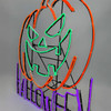 Lit up bright neon Halloween sign featuring a glowing orange pumpkin with a green jack‑o’‑lantern face and purple ‘Halloween’ text on a black background.