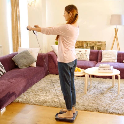Person standing barefoot on the Omron BF511 digital scale and holding the connected handles forward to perform a full-body measurement.