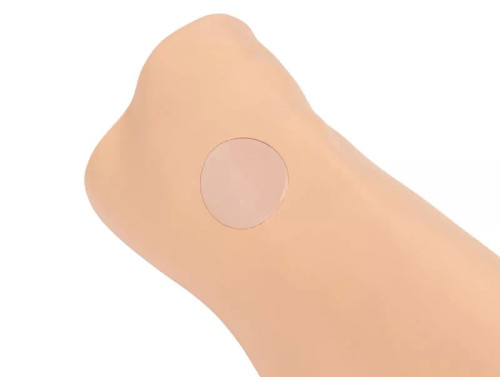 Close-up view of a simulated lower leg showing the circular replaceable intraosseous (IO) puncture pad on the tibial insertion site.