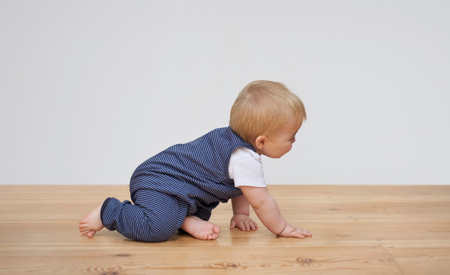 Baby crawling barefoot on a wooden floor