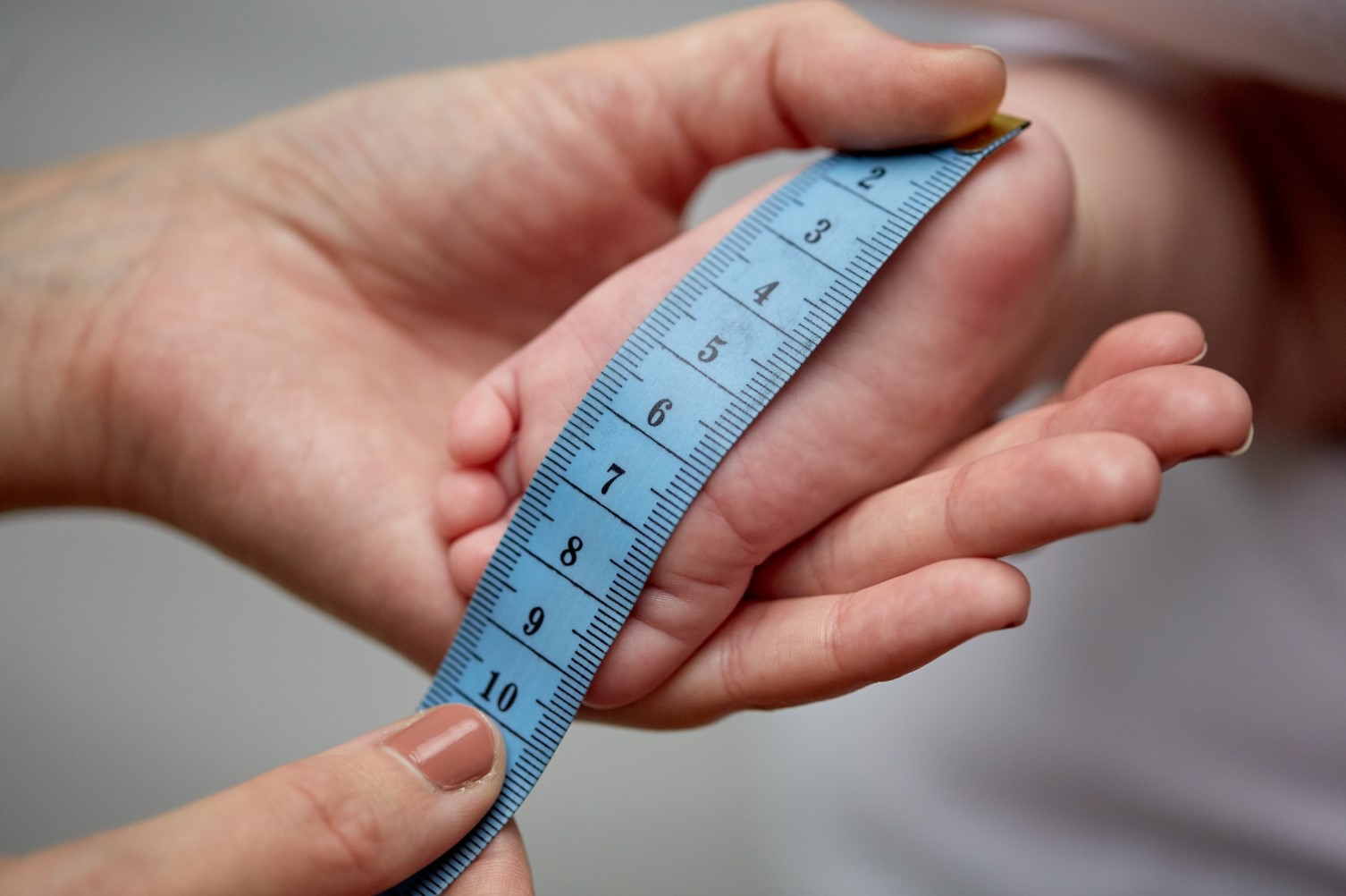 A close up of hands measuring a baby’s foot with a tape measure.