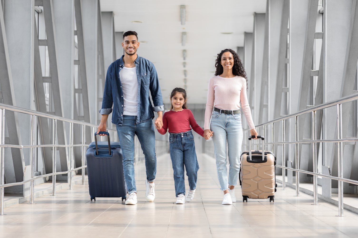 A young girl and her parents walk through the corridor at an airport, ready to go on holiday.