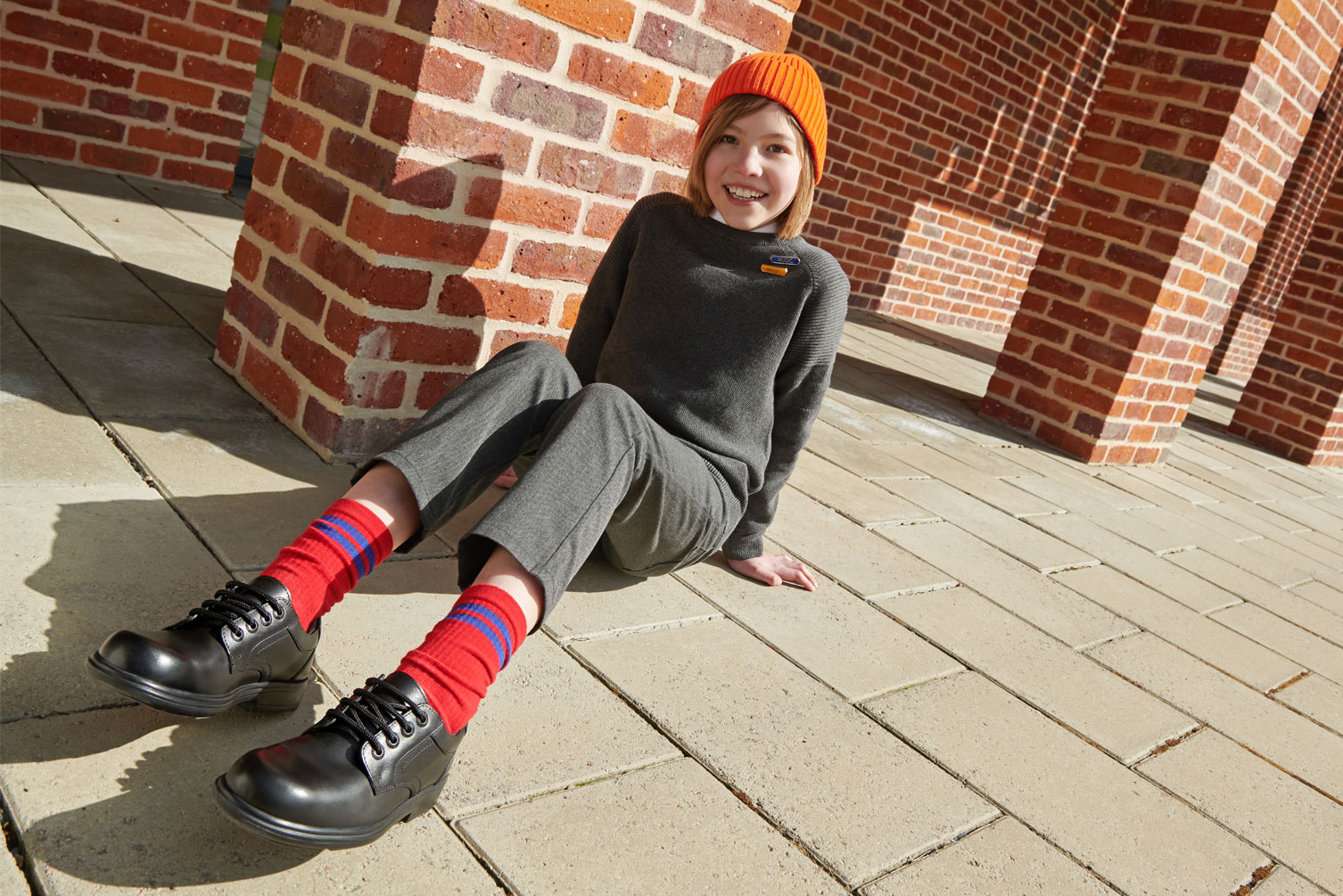 The best school shoes for wide feet Smiling boy sitting in school uniform, wearing Start-Rite school shoes with red socks and a yellow beanie hat