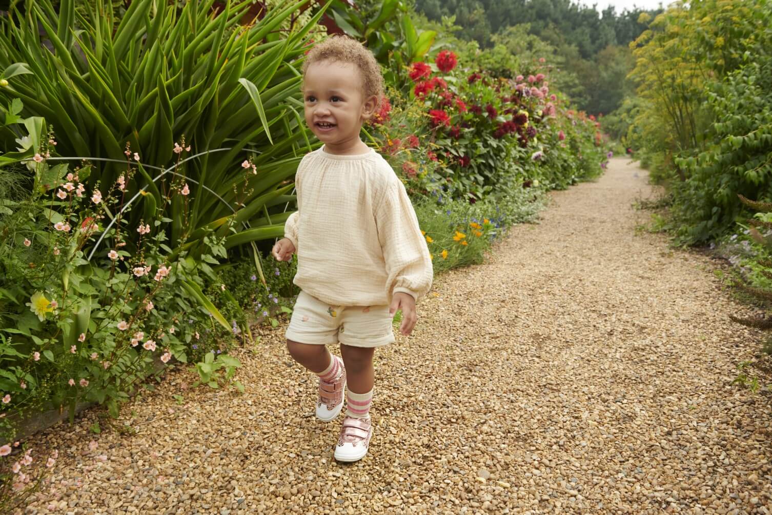 Girl wearing Start-Rite shoes running through a garden on a gravel path