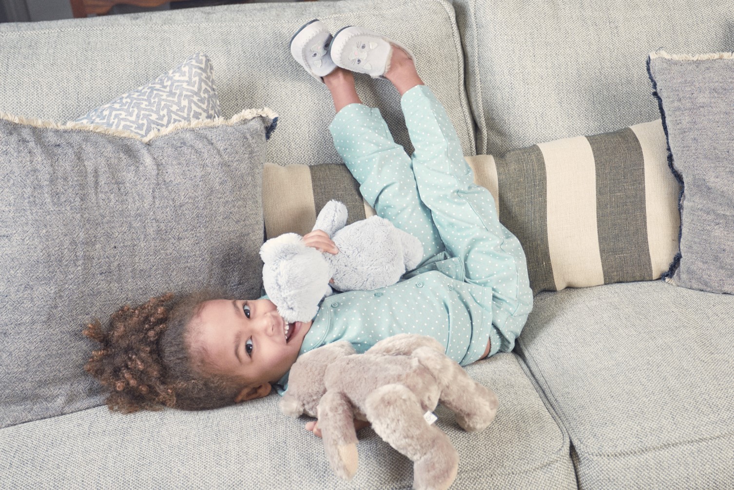 a young girl wearing slippers lays on the sofa smiling