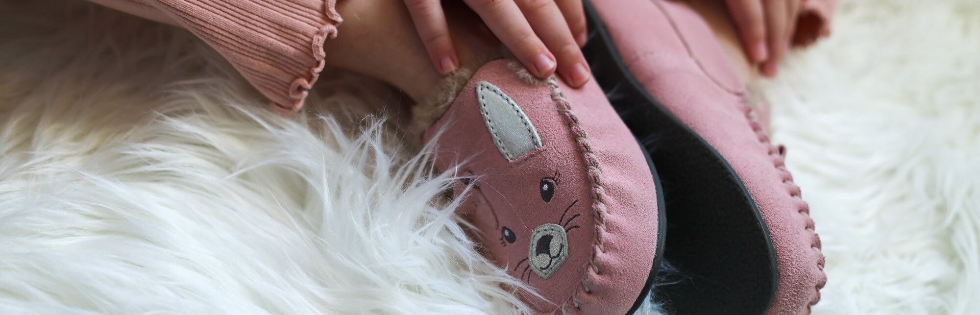 a girl sitting, wearing slippers and cupping her feet in her hands