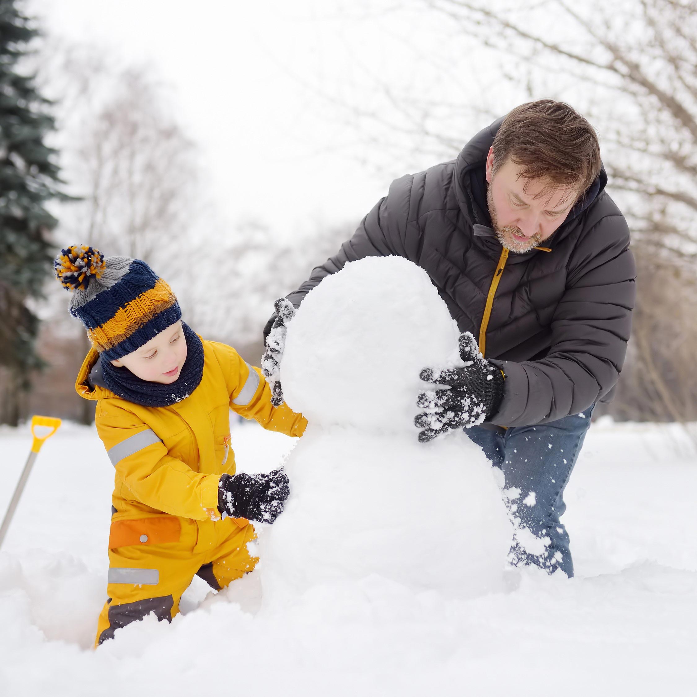 a little boy and his dad building a snowman together