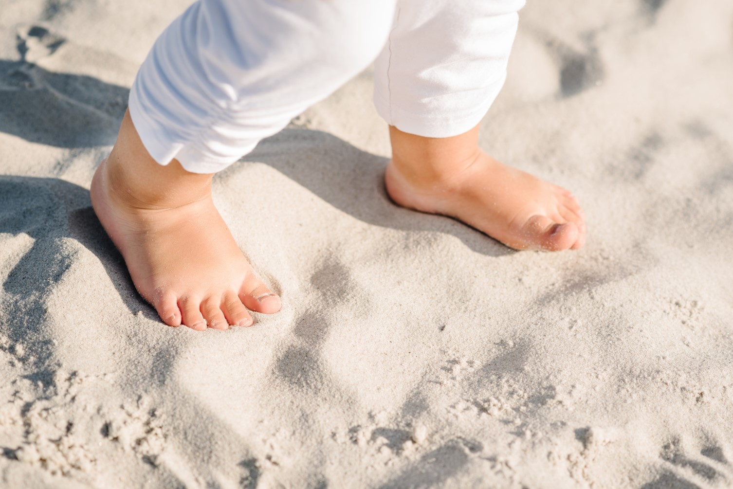 a toddler with flat feet walks barefoot on a sandy beach