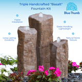 Triple handcrafted basalt fountain kit with three stone columns emitting water. Surrounding pink and white flowers add vibrant contrast. Features, like durability and lightweight design, are highlighted.